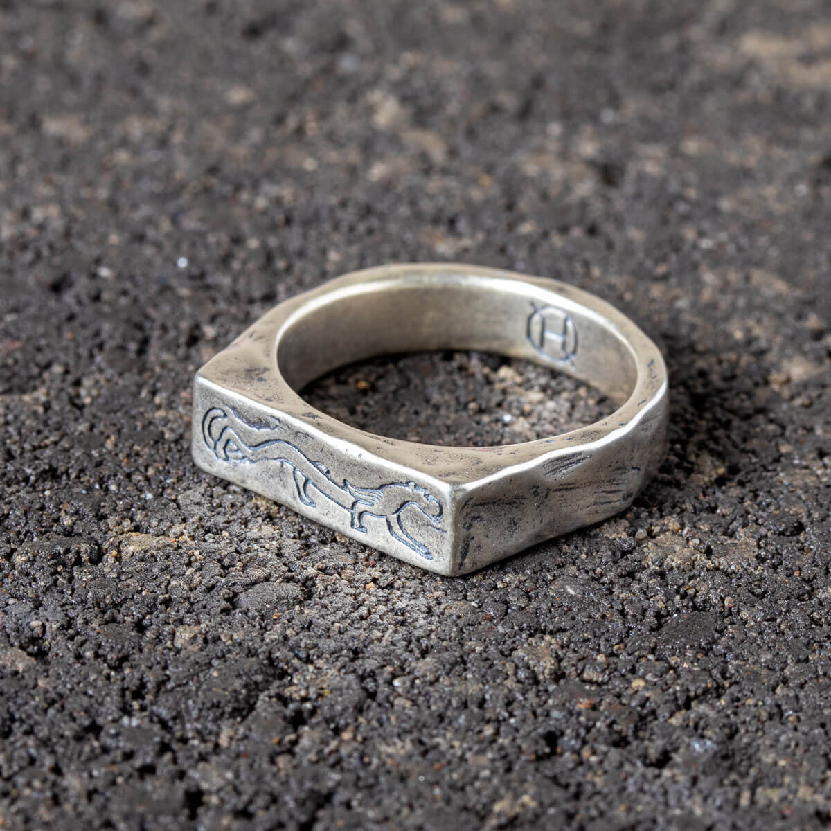 Silver ring with engraved panther design on a dark textured surface - angled view