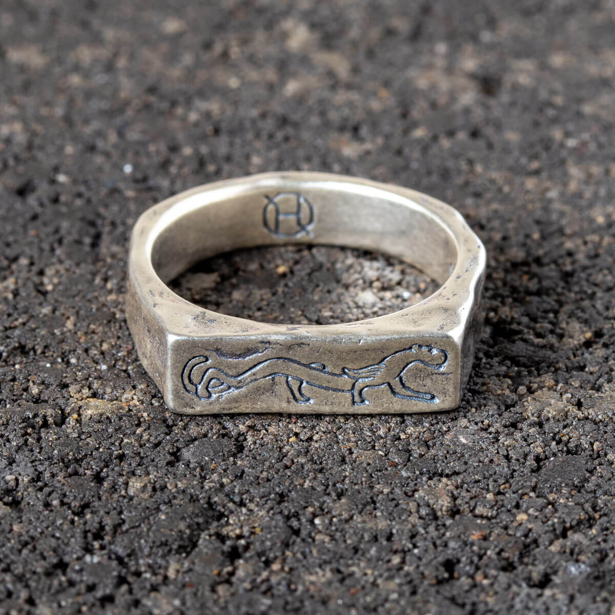 Silver ring with engraved panther design on a dark textured surface