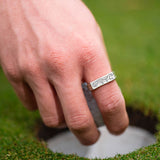 Hand wearing a silver ring with a design on a grassy background