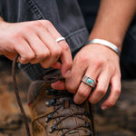 Person tying a hiking boot with close-up of hands and rings.
